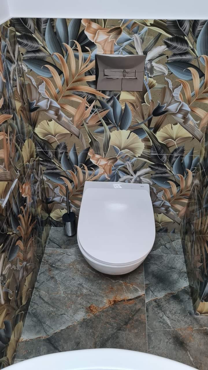 Wykończona łazienka z toaletą na tle ściany w kwiatowy wzór i szarej marmurowej podłogi z brązowymi żyłkami. Widoczny dozownik mydła i szczotka do WC.