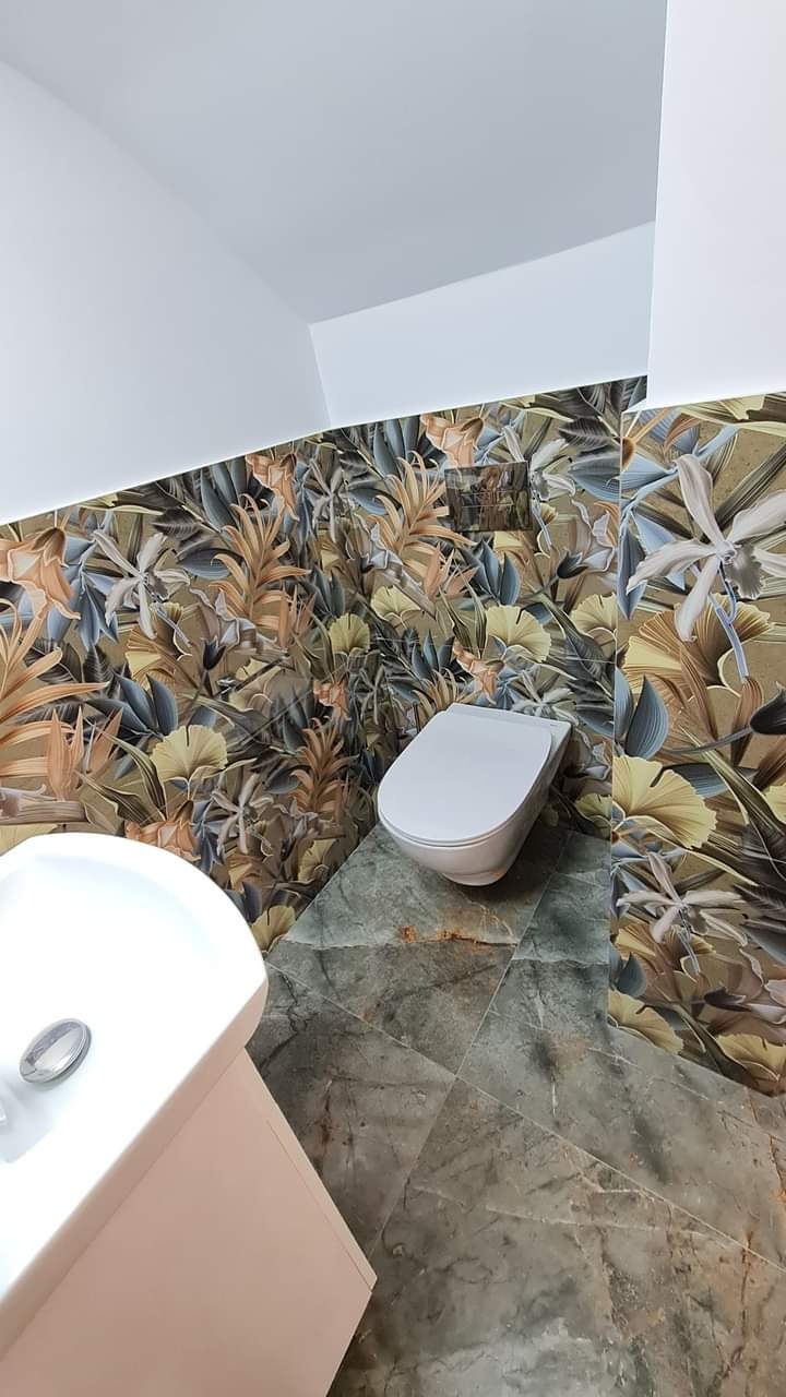 Wykończona łazienka z umywalką, toaletą i płytkami w kwiatowy wzór na ścianach oraz marmurową posadzką. Nietypowe połączenie wzorów i materiałów.