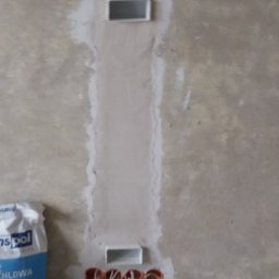 VolTS - Usługi Elektryczne Tomasz Sterniak - Bruzda w ścianie po instalacji elektrycznej, z widocznymi puszkami i przewodami, przygotowana do szpachlowania. Obok worek gipsu.