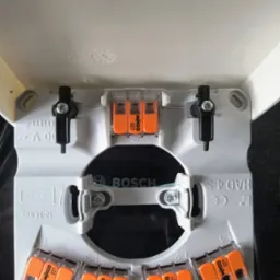 Szara puszka instalacyjna Bosch z pomarańczowymi złączkami Wago 221, widok z góry. Złączki rozmieszczone wewnątrz puszki, gotowe do podłączenia przewodów.