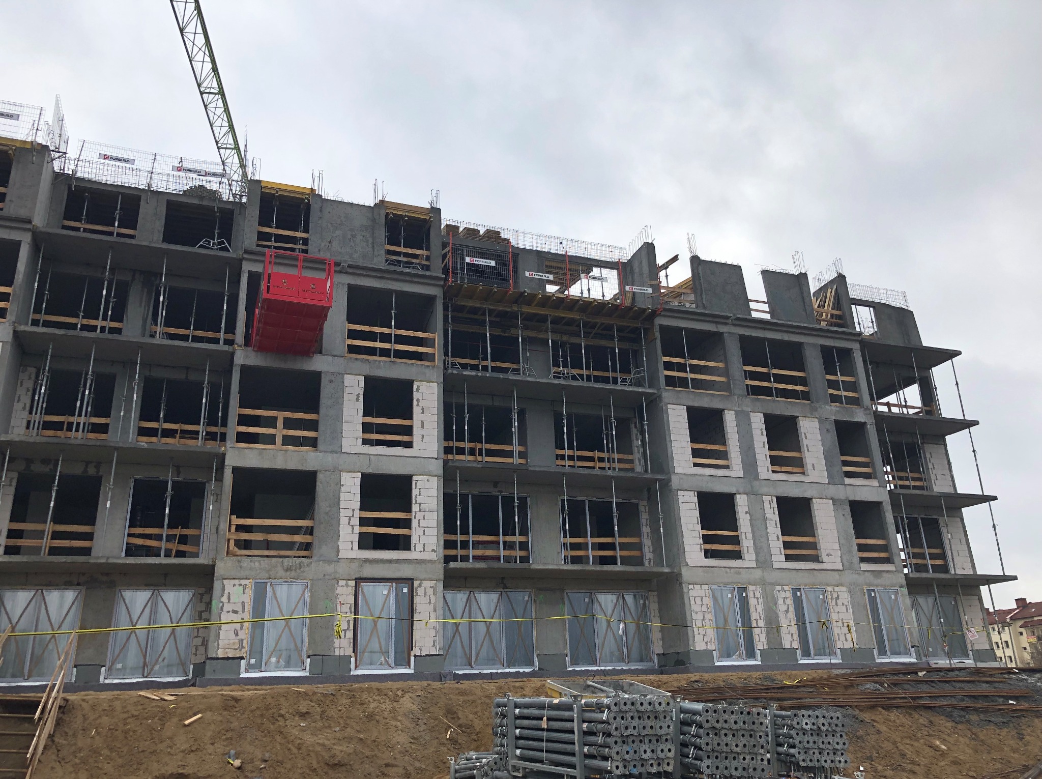 Budowa budynku wielorodzinnego w stanie surowym otwartym. Widoczny żuraw, szalunki i podpory. Budynek z betonu komórkowego z oknami na parterze.