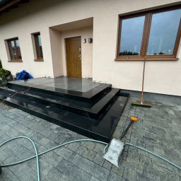 Prof-bruk - Nowoczesne, czarne schody z kostki, prowadzące do domu z numerem 3. Widoczna ułożona kostka brukowa, narzędzia pracy: łopata, szczotka, wiadro i wąż ogrodowy.