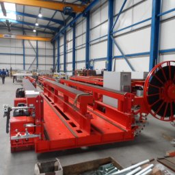 DIEFFENBACHER MASCHINENFABRIK SPÓŁKA Z OGRANICZONĄ ODPOWIEDZIALNOŚCIĄ - Czerwona, stalowa konstrukcja w hali produkcyjnej z suwnicą. Widoczne elementy złączne i niebieskie elementy konstrukcyjne hali.