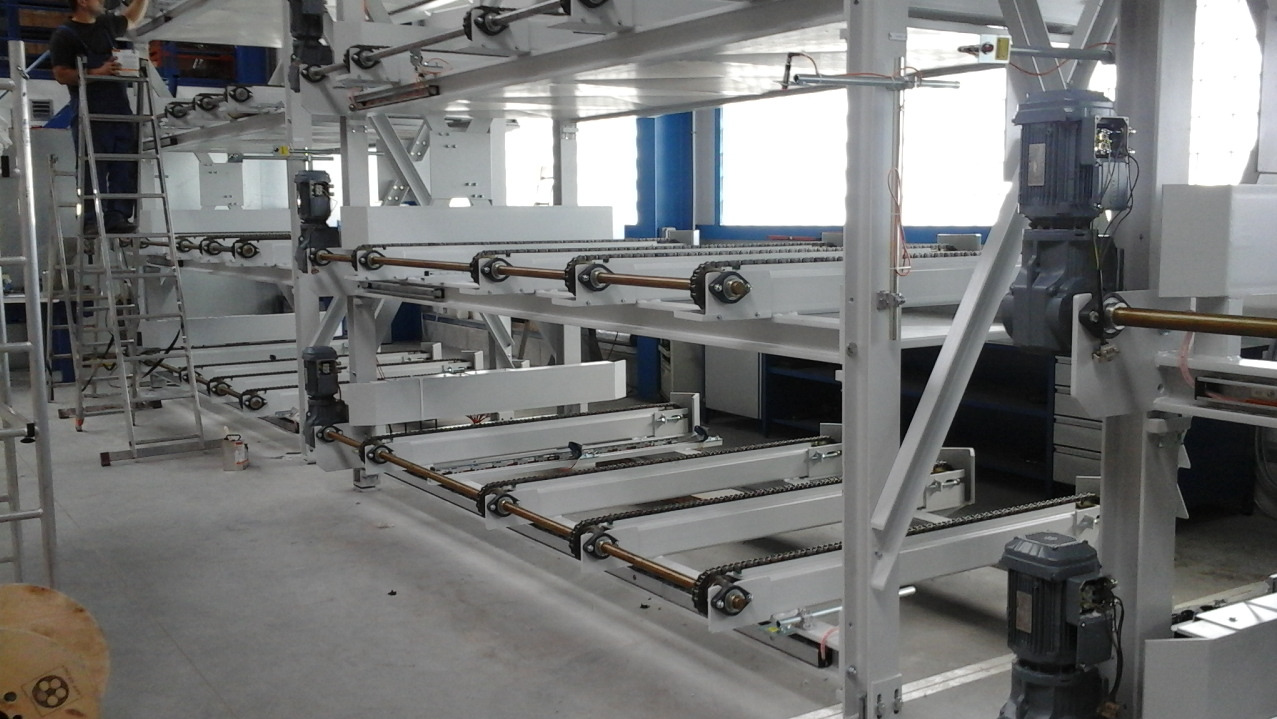 Konstrukcja stalowa z łańcuchami transportowymi, biała, wielopoziomowa, widoczna osoba na drabinie. Realizacja z Kościana.