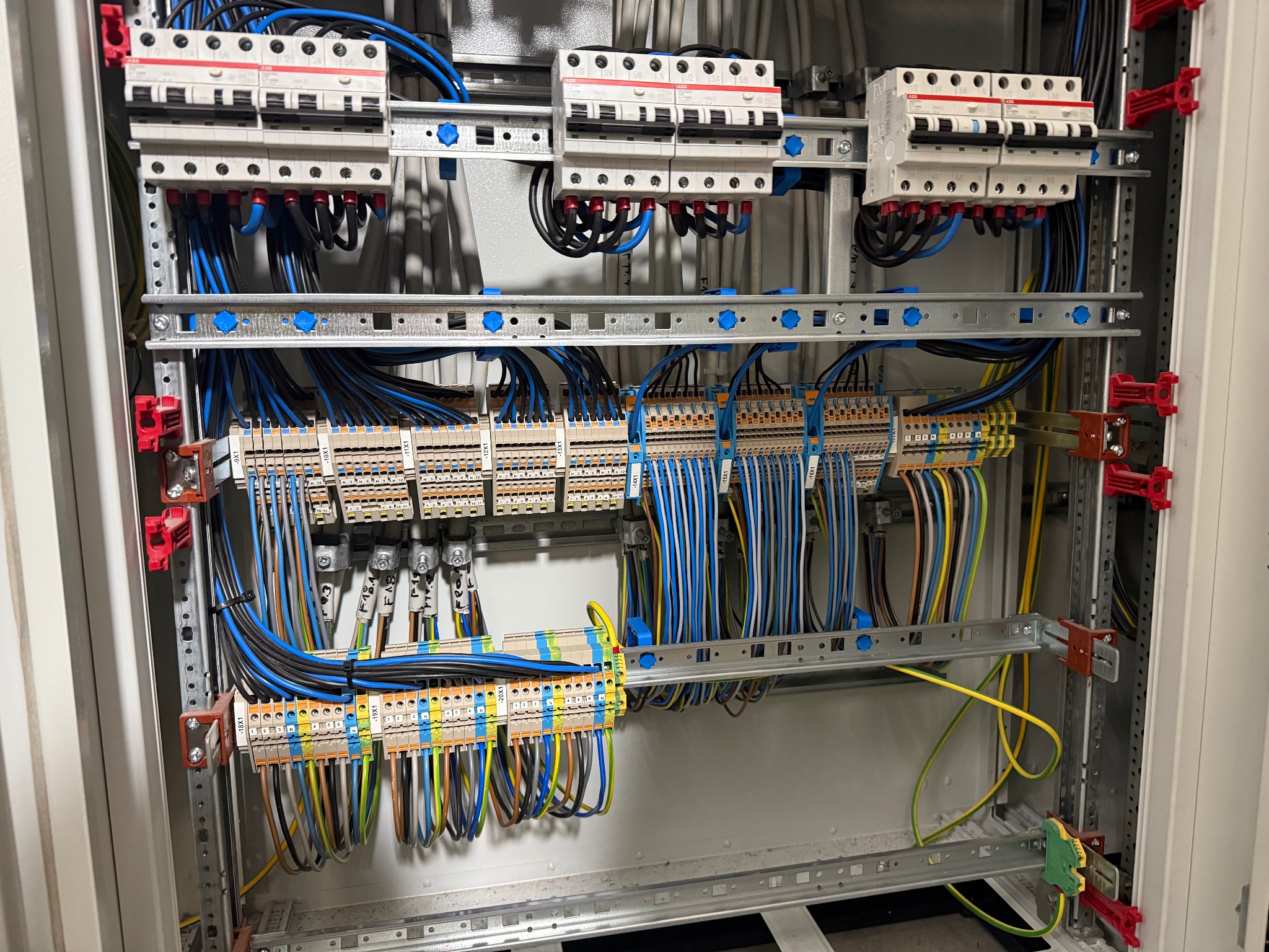 Rozdzielnica elektryczna z bezpiecznikami, listwami zaciskowymi i okablowaniem w kolorach niebieskim, czarnym, żółto-zielonym. Widok z bliska, wewnątrz szafy rozdzielczej.