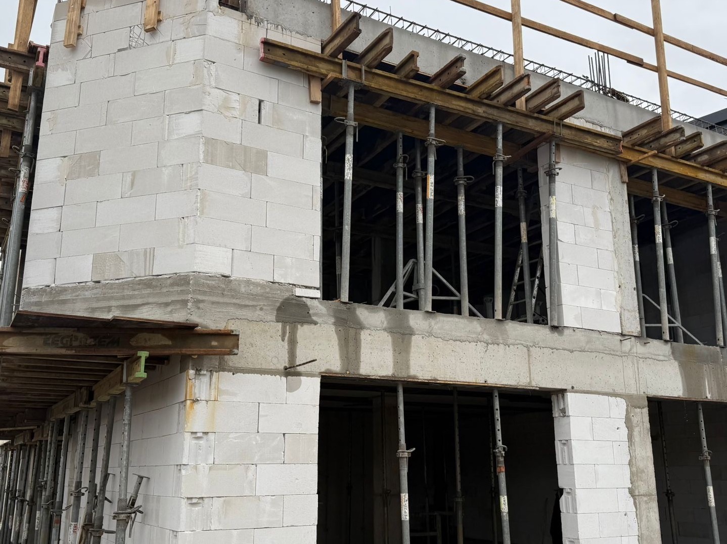 Surowy stan budynku z białych bloczków, z widocznym zbrojeniem i podporami, ukazujący etap budowy domu. Widoczne drewniane elementy szalunku.