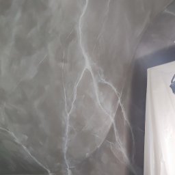 LOFTDEKOR SPÓŁKA Z OGRANICZONĄ ODPOWIEDZIALNOŚCIĄ - Ściana i sufit wykończone szarym mikrocementem z białymi żyłkami imitującymi marmur, częściowo zasłonięte folią ochronną podczas prac wykończeniowych.