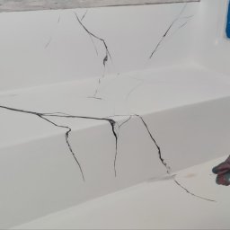 LOFTDEKOR SPÓŁKA Z OGRANICZONĄ ODPOWIEDZIALNOŚCIĄ - Biała powierzchnia z imitacją czarnych żyłkowania marmuru, wykonywana ręcznie. Fragment malowanej ściany z niebieską taśmą malarską. Detal dłoni malarza.