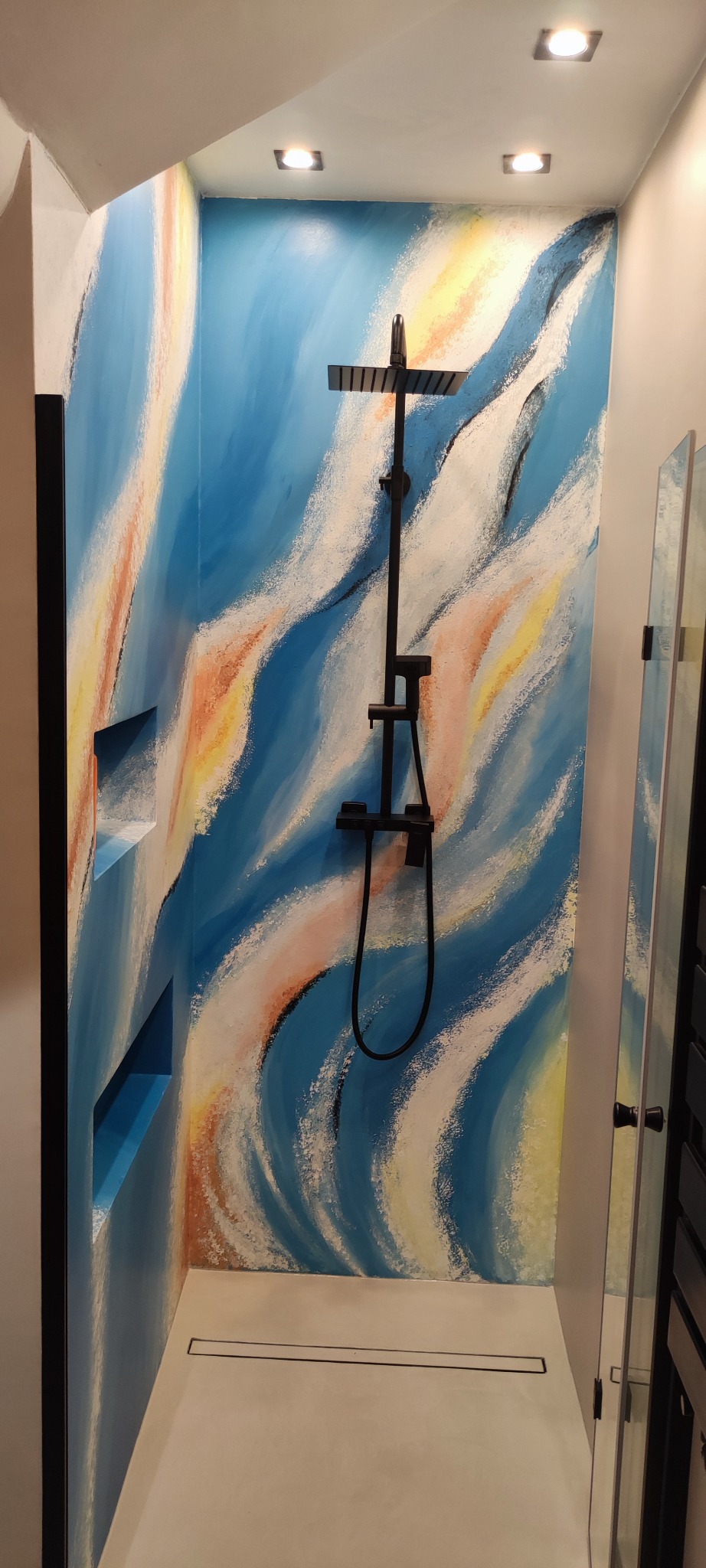 Nowoczesna kabina prysznicowa z abstrakcyjnym malowaniem ścian w odcieniach błękitu i beżu. Czarna armatura i wnęki w ścianie dodają charakteru.