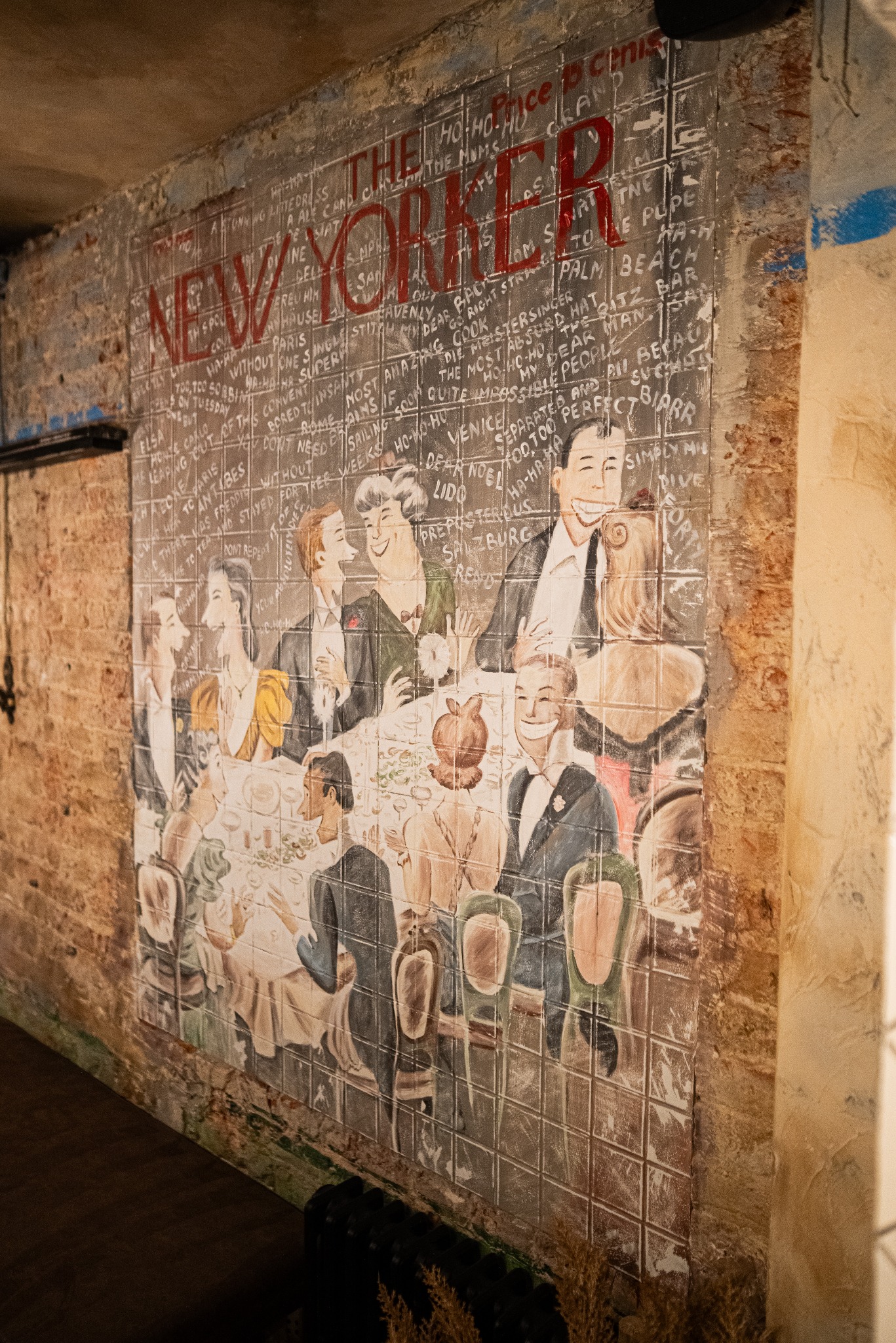 Ściana z płytek ceramicznych zdobiona rysunkiem w stylu retro, przedstawiającym scenę towarzyską z napisem 'New Yorker'. Nietypowe wykończenie wnętrza.