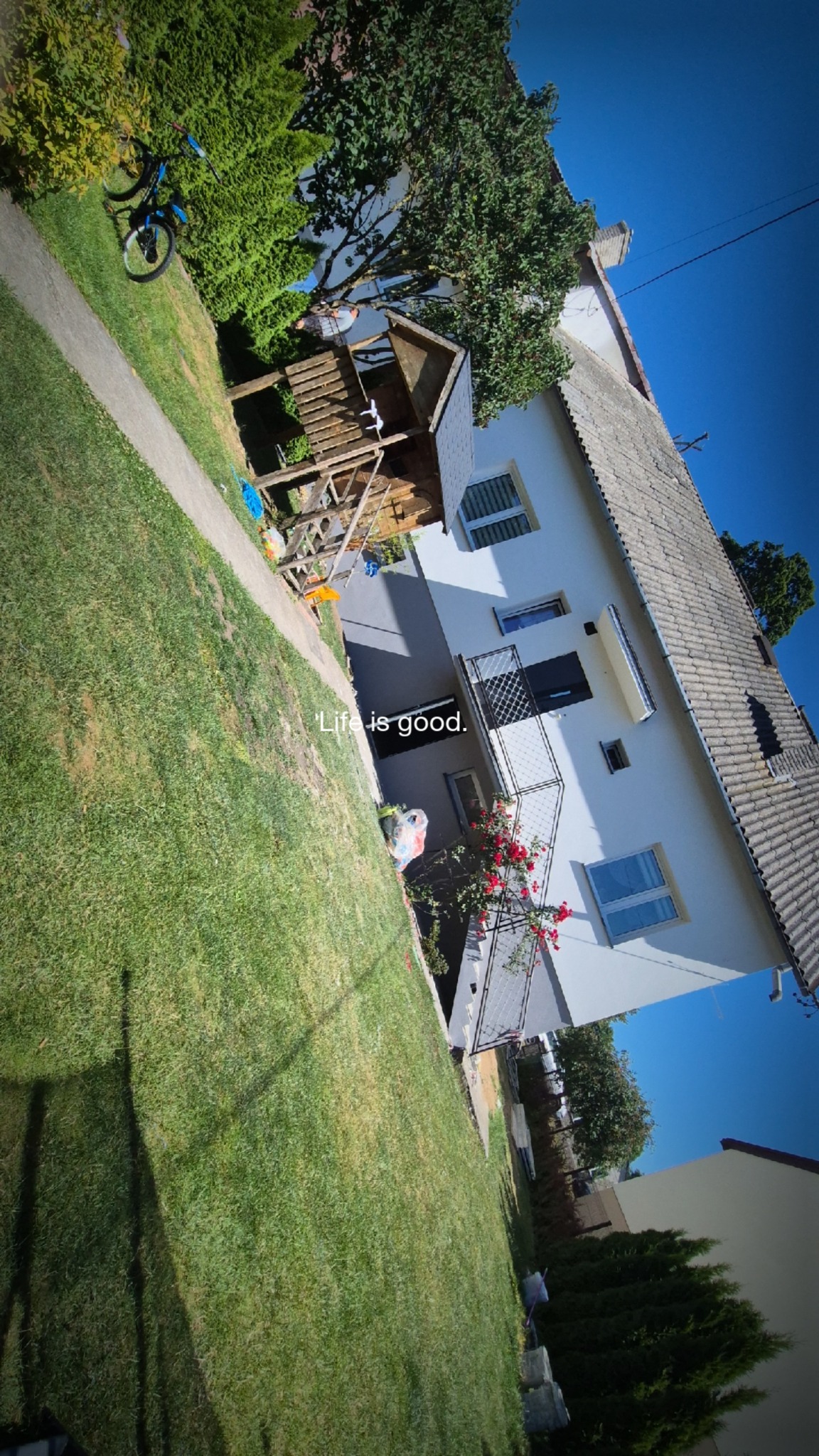 Dwupiętrowy dom jednorodzinny z szarą elewacją po remoncie, widok z zewnątrz na ogród z placem zabaw dla dzieci.