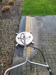 Mycie kostki brukowej myjką ciśnieniową. Częściowo umyta powierzchnia kostki, widoczna różnica w kolorze. Obok trawnik i rabata z korą.