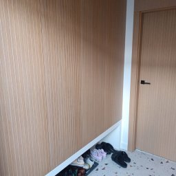 VERTIKA S.C. - Szafa wnękowa z drewnianymi lamelami i miejscem na buty, z widocznymi butami na podłodze z terazzo w przedpokoju. Minimalistyczny design.