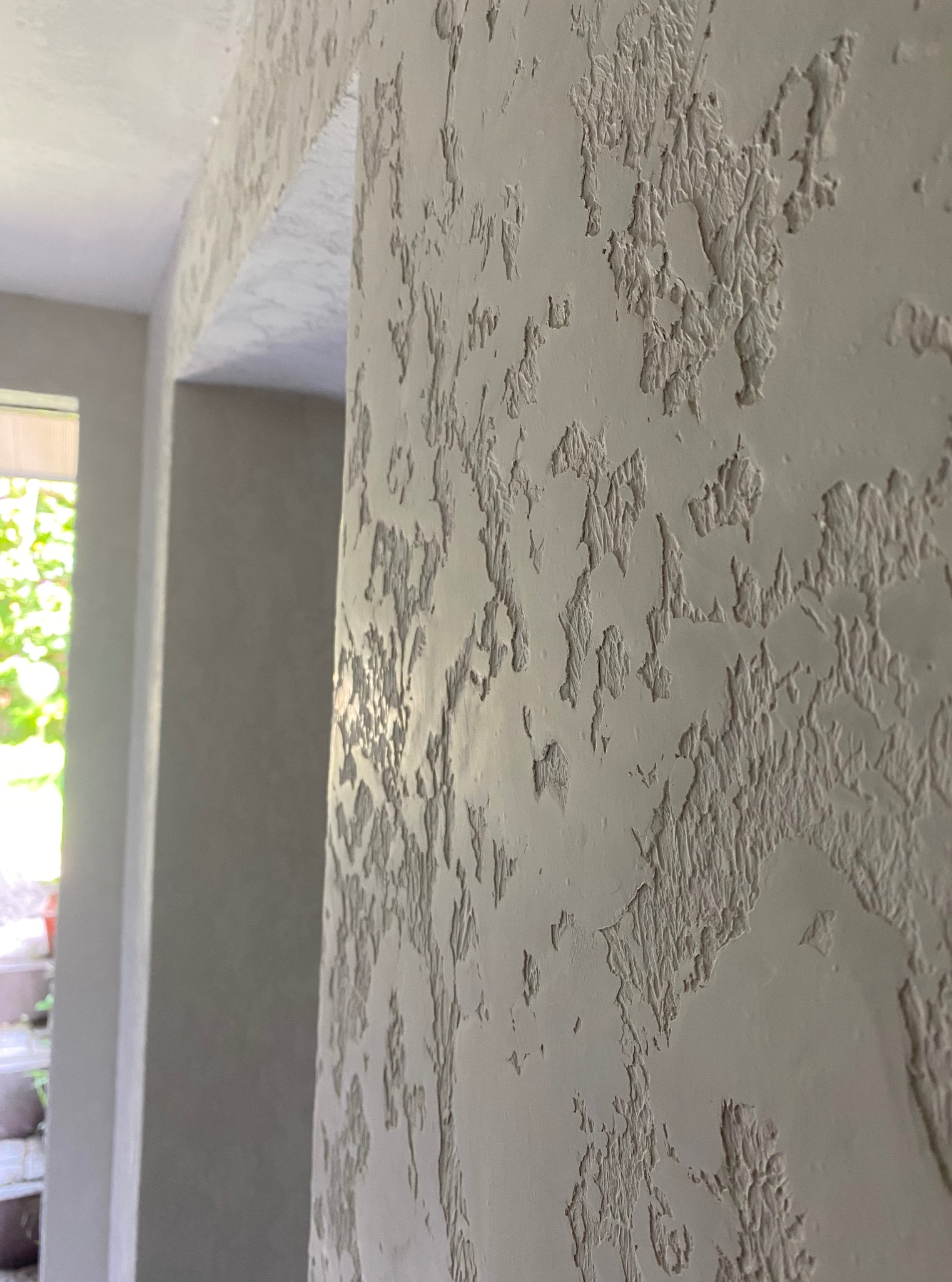 Dekoracyjna ściana z wyraźną fakturą w odcieniach szarości, widoczny fragment przejścia do innego pomieszczenia. Specyficzny wzór na ścianie, światło dzienne.