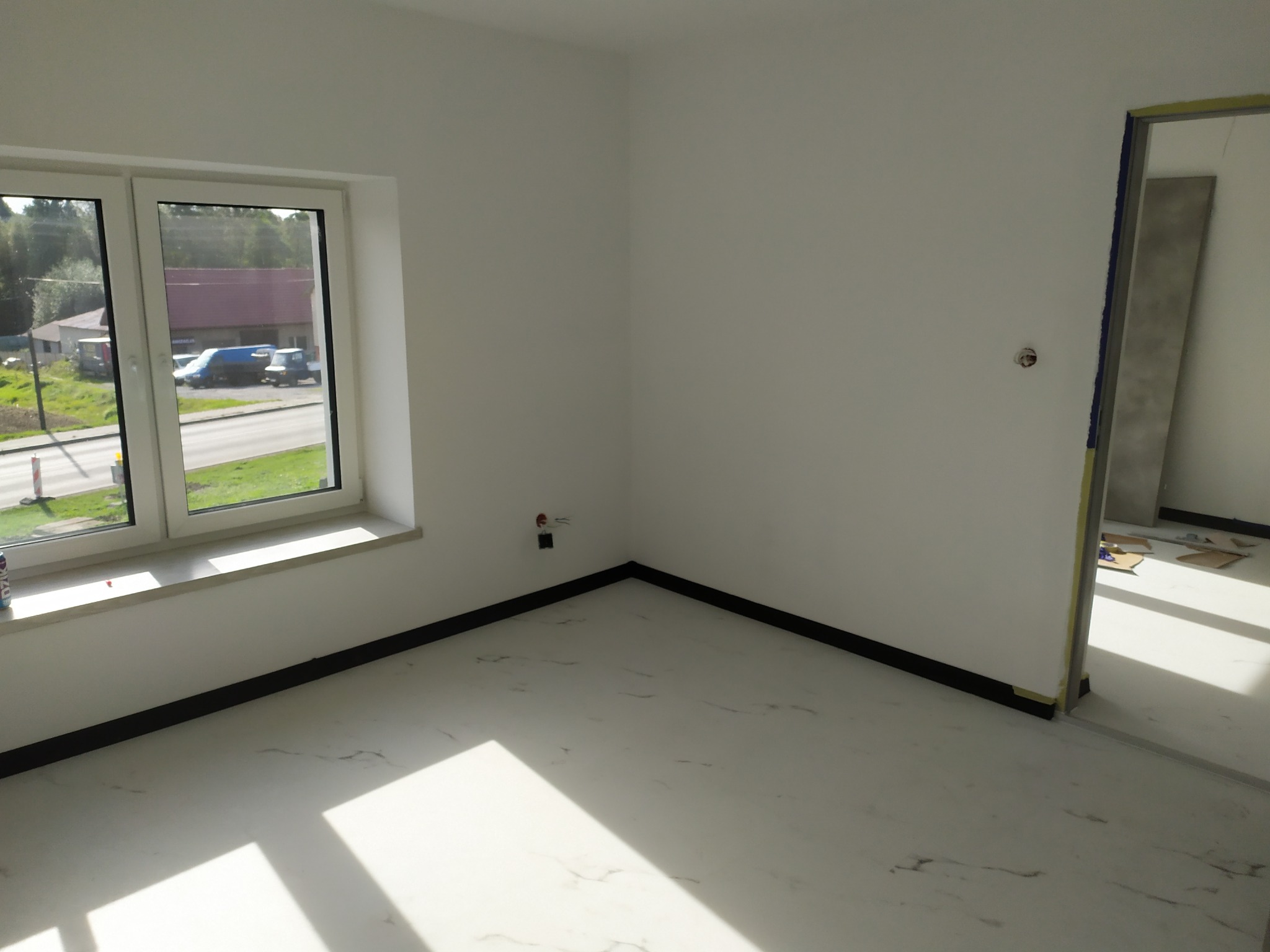 Jasne, puste wnętrze po remoncie: białe ściany, marmurowe podłogi, okno z widokiem na zewnątrz i przygotowane wejście do kolejnego pomieszczenia.