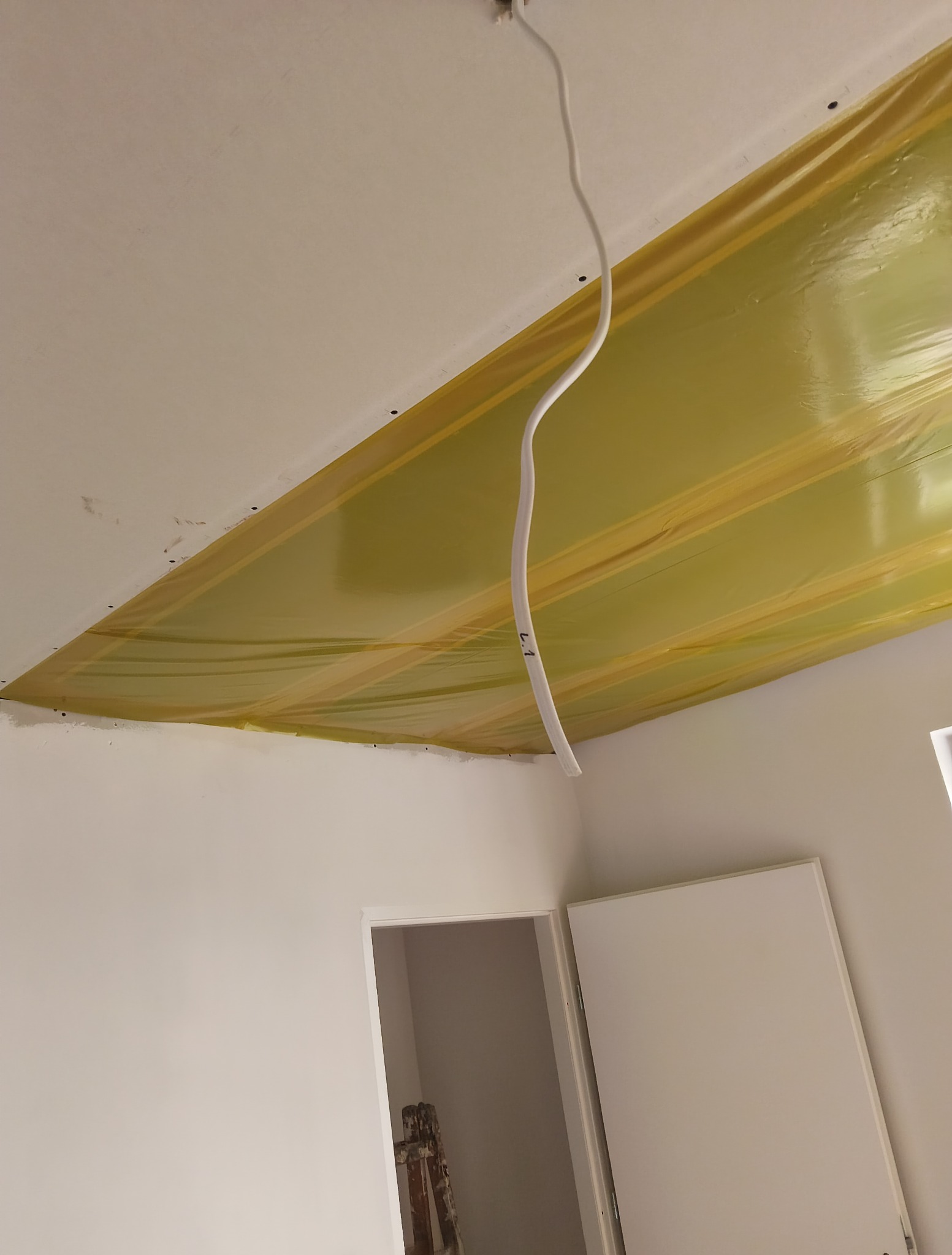 Przygotowanie sufitu do montażu płyty KG: widoczna folia paroizolacyjna, wystający przewód elektryczny. W tle fragment ściany i drzwi.