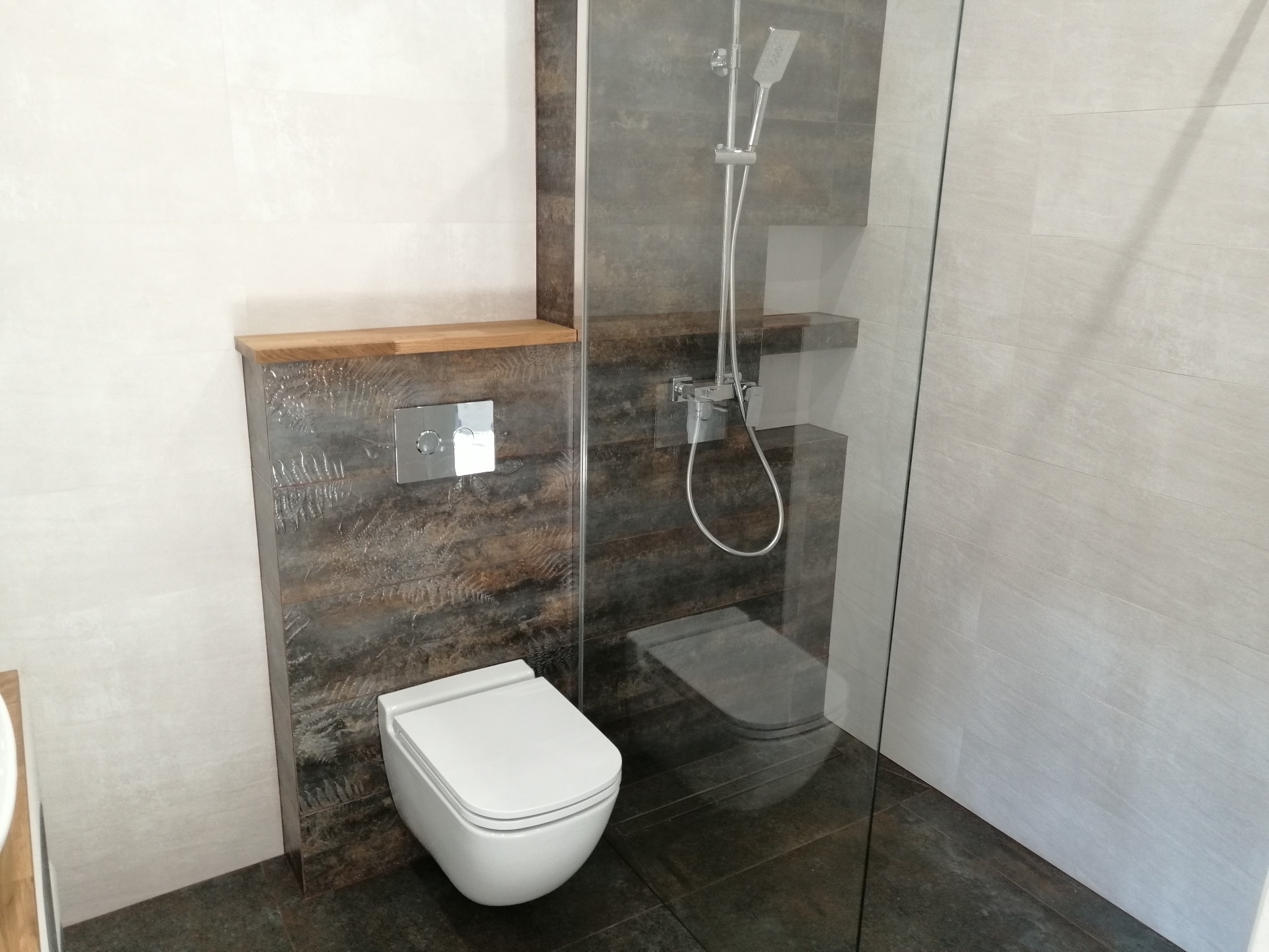 Nowoczesna łazienka z kabiną prysznicową typu walk-in, podwieszaną toaletą i płytkami imitującymi drewno. Minimalistyczny design z akcentami naturalnego drewna.