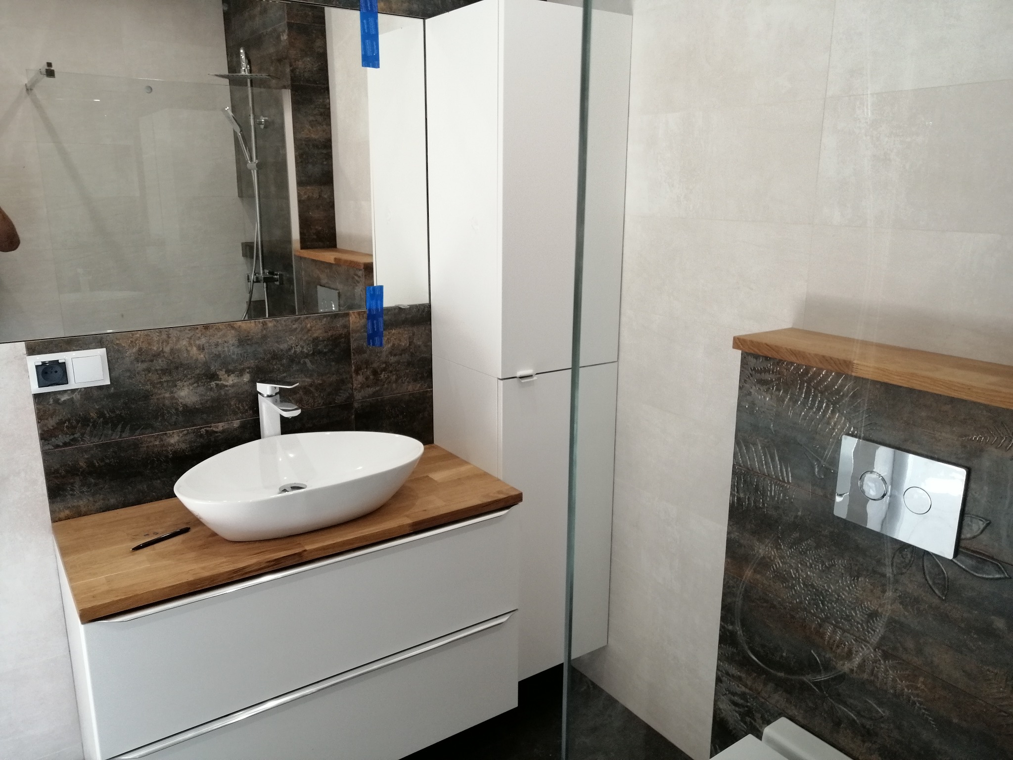 Nowoczesna łazienka po remoncie: biała umywalka nablatowa na drewnianym blacie, szafka pod umywalką, kabina prysznicowa ze szkła, płytki imitujące drewno.