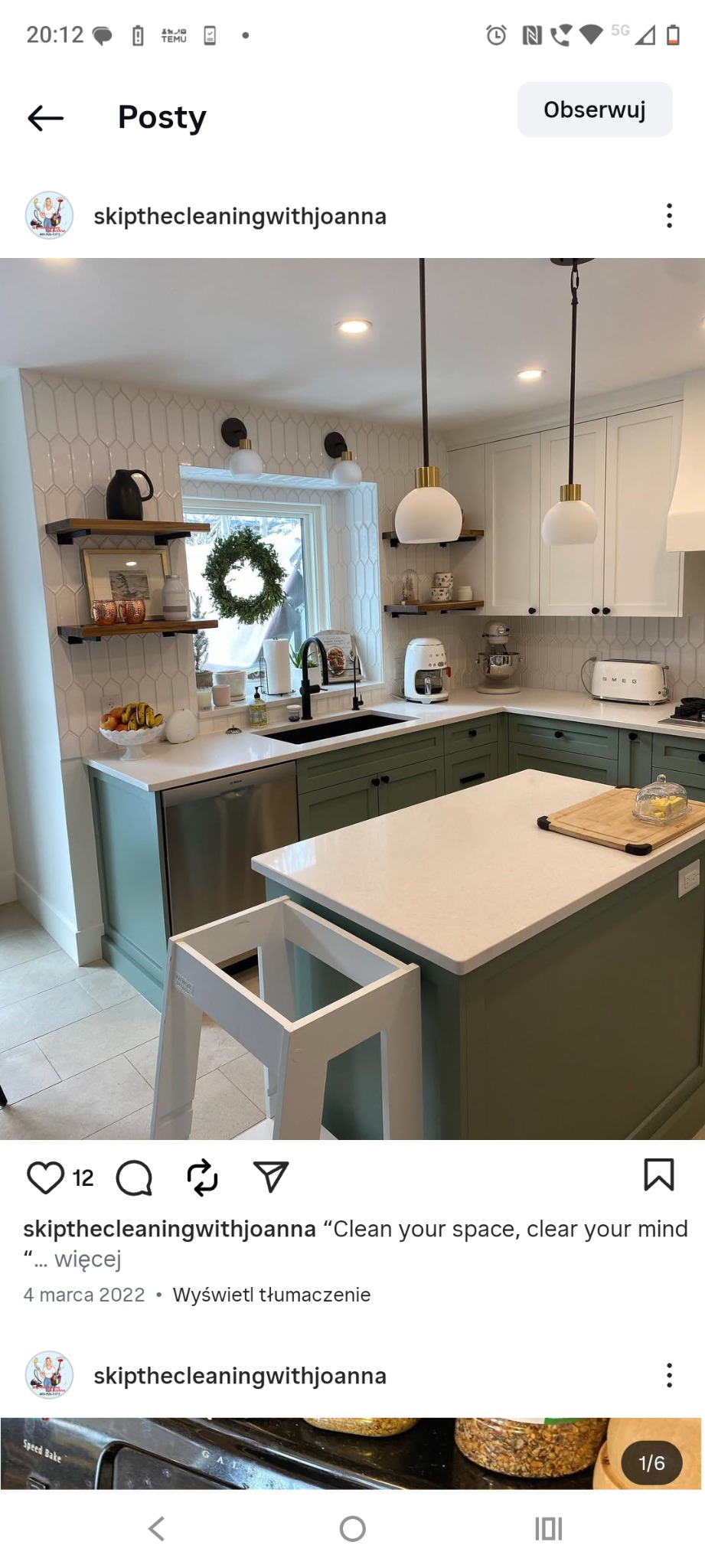 Kuchnia w stylu retro z zielonymi szafkami, białymi blatami i wyspą. W tle okno z dekoracyjnym wieńcem. Widoczny podest.