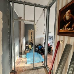 Remontivo - Montaż metalowej konstrukcji ścianki działowej z płyt gipsowo-kartonowych w trakcie remontu wnętrza. Widoczne profile, poziomica i narzędzia.