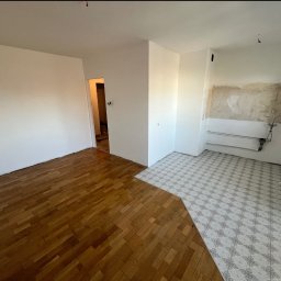 Remontivo - Fragment wnętrza po remoncie: parkiet w pokoju i wzorzysta podłoga w kuchni, świeżo pomalowane ściany. Widoczne kable i rury, stan po częściowym remoncie.