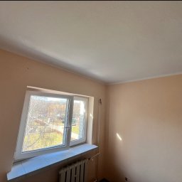 Remontivo - Jasny pokój po odświeżeniu ścian w odcieniach beżu. Widoczne okno z widokiem na zewnątrz i grzejnik pod nim. Na suficie widoczny punkt oświetleniowy.