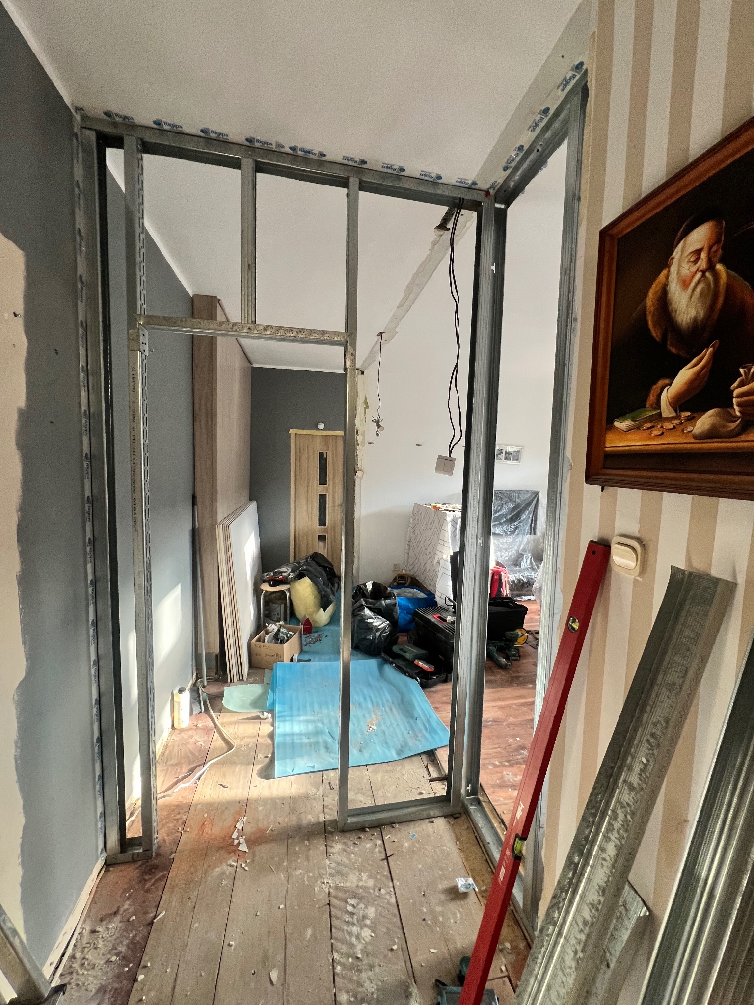 Montaż metalowej konstrukcji ścianki działowej z płyt gipsowo-kartonowych w trakcie remontu wnętrza. Widoczne profile, poziomica i narzędzia.