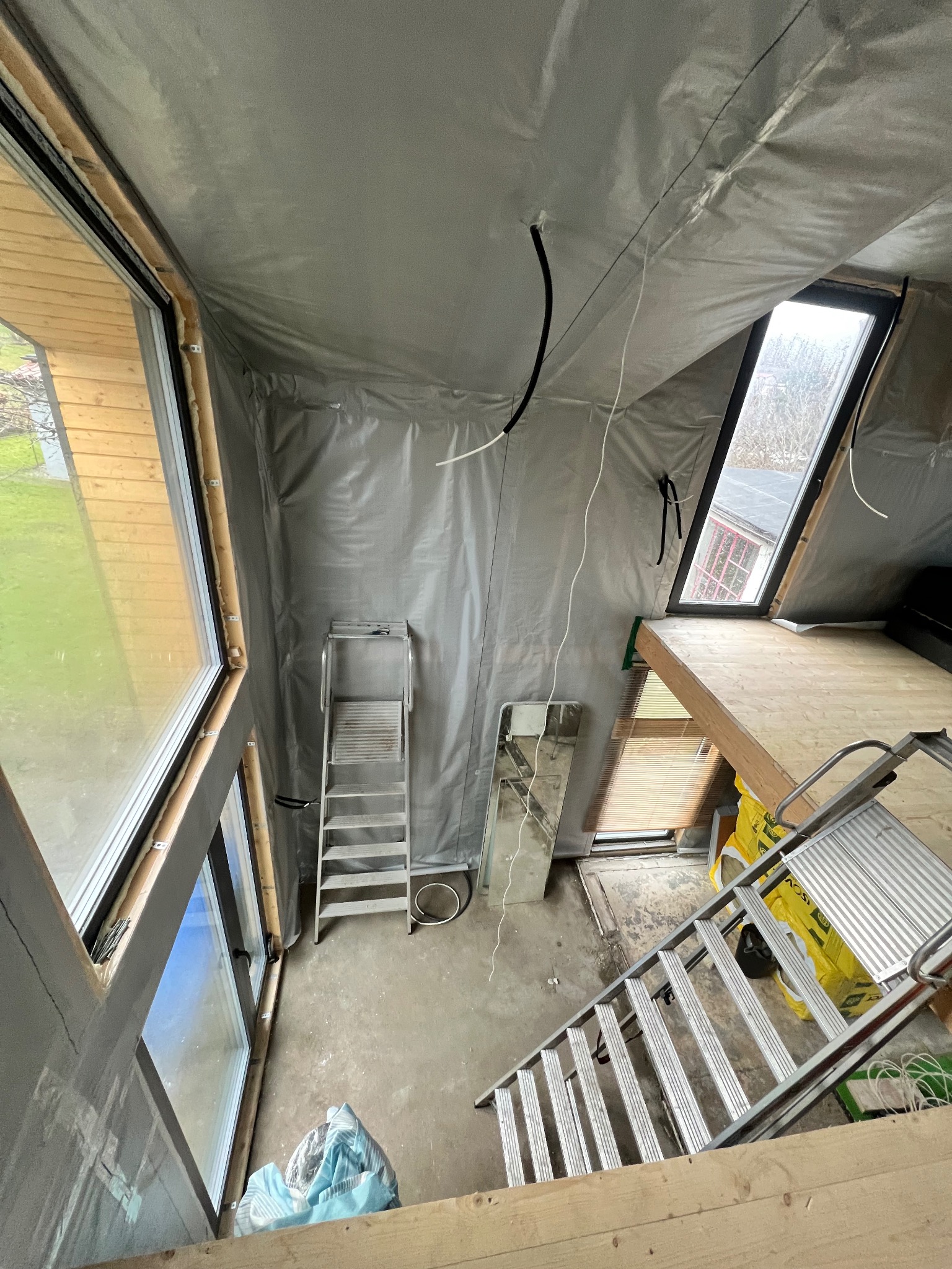 Skośne poddasze w trakcie prac przygotowawczych w Sopocie. Folia ochronna na ścianach, drabiny, okna dachowe i pionowe. Widok z góry na remontowane wnętrze.