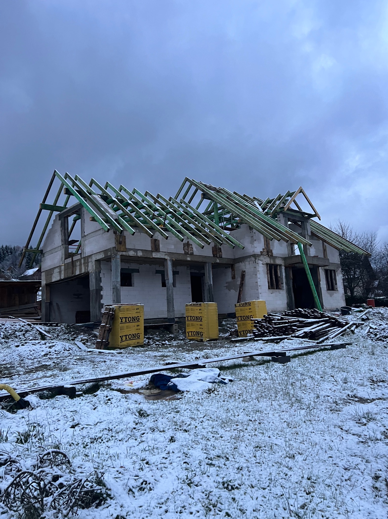 Wznoszenie domu z bloczków Ytong w zimowej scenerii Jaworzynki. Widoczna konstrukcja dachu z zielonych belek, śnieg na ziemi i częściowo otynkowane ściany.