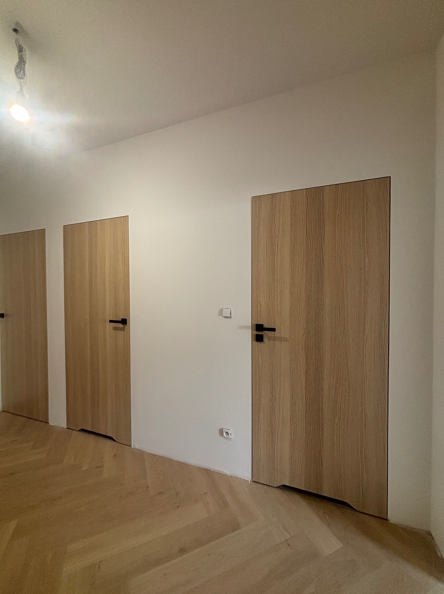 Wykończone wnętrze w Katowicach: trzy drewniane drzwi z czarnymi klamkami, parkiet ułożony w jodełkę, świeżo pomalowane ściany w jasnym odcieniu.