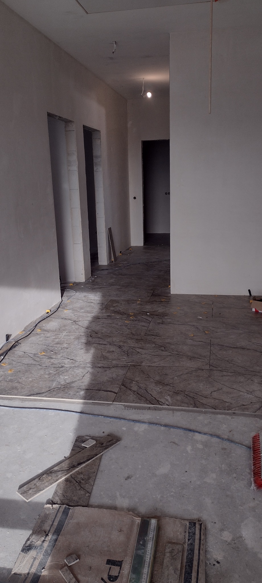 Układanie płytek podłogowych w odcieniach szarości z marmurkowym wzorem w nowym wnętrzu. Widoczne krzyżyki dystansowe i narzędzia glazurnicze.