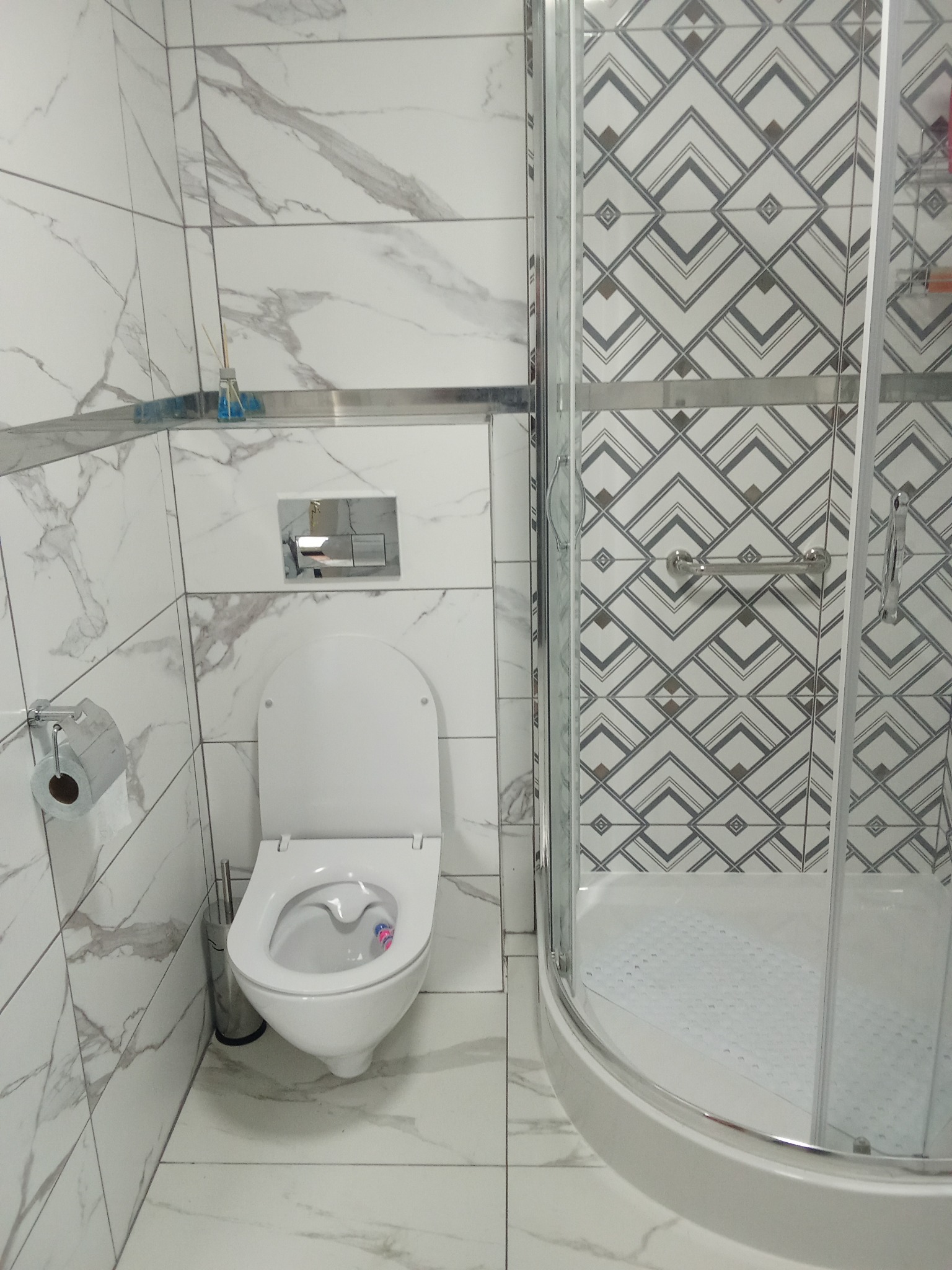 Wykończona łazienka w Cieszkowie: białe płytki imitujące marmur, kabina prysznicowa z geometrycznym wzorem, toaleta. Nowoczesny design.