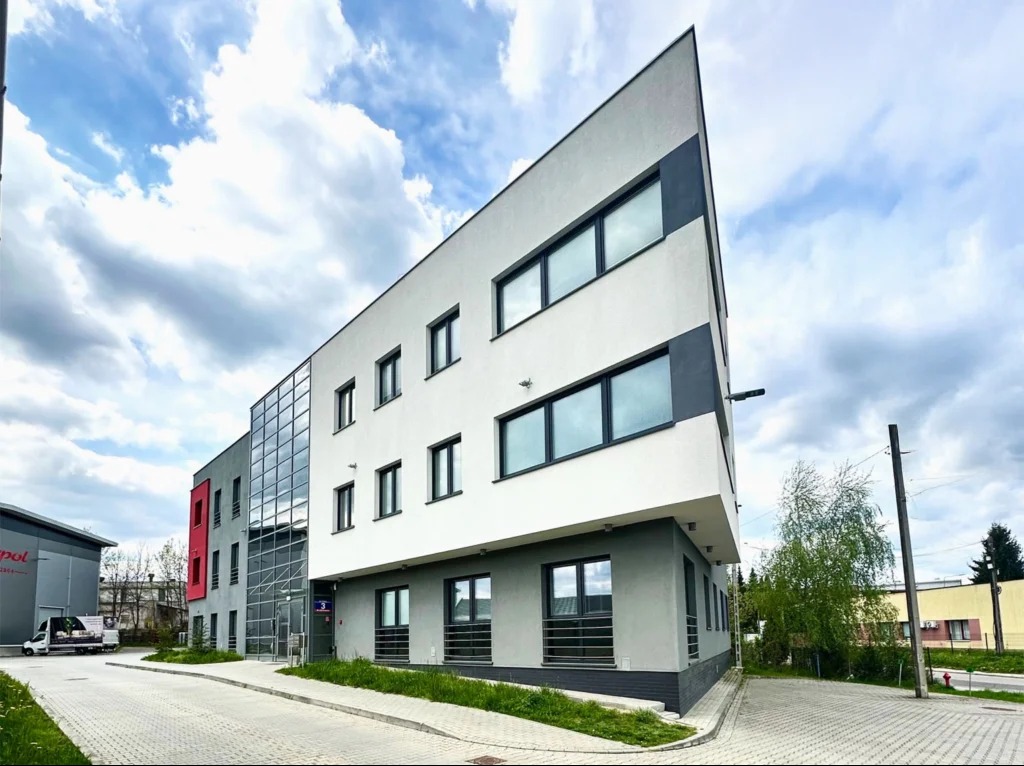 Nowoczesny budynek biurowy z jasną elewacją i geometryczną formą, zlokalizowany w Rzeszowie, Polska. Widok z poziomu chodnika, błękitne niebo z chmurami w tle.