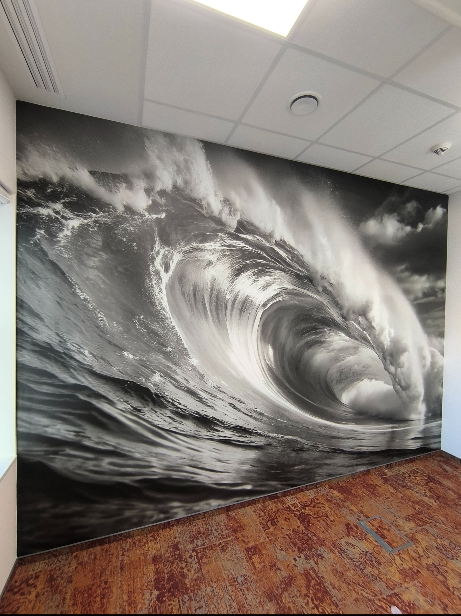 Fototapeta z motywem wzburzonego morza zdobi ścianę biura w Warszawie. Czarno-biała grafika z efektem głębi, widoczna struktura i faktura tapety.