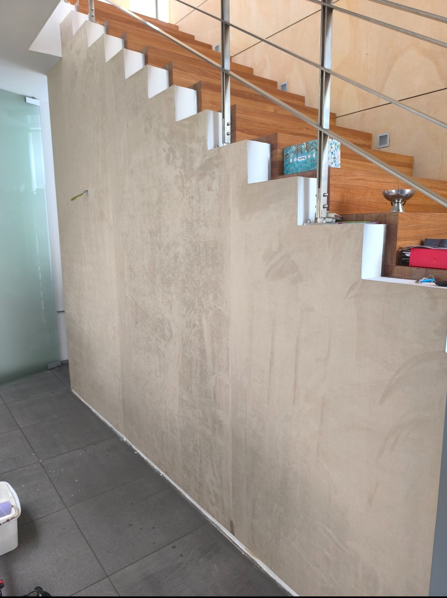 Wykończona ściana z efektem dekoracyjnym w odcieniach beżu, przylegająca do schodów z drewnianymi stopniami i metalową balustradą, widok z dołu.