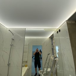 Viktor Yevsiukov - Wykończona łazienka z marmurowymi płytkami i podświetlanym sufitem, widoczna drabina i odbicie osoby robiącej zdjęcie w dużym lustrze.