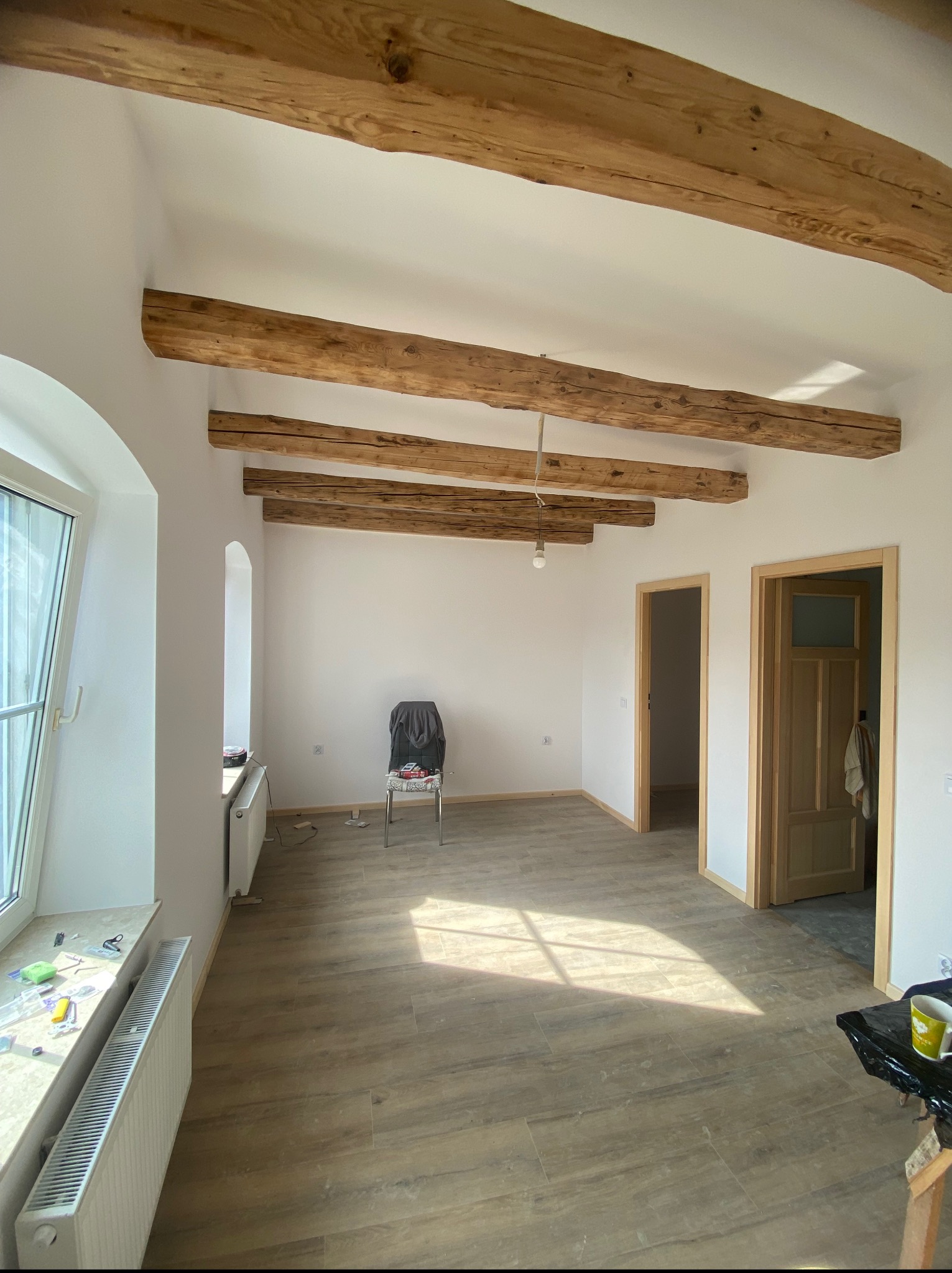 Jasne wnętrze z drewnianymi belkami stropowymi i dwiema parami drzwi z drewnianymi futrynami. Podłoga wyłożona panelami imitującymi drewno.