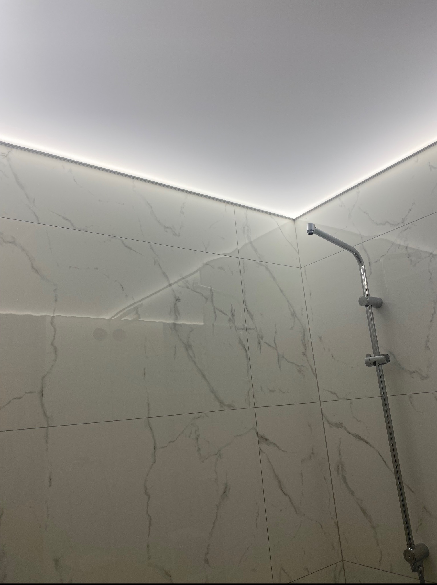 Wykończona łazienka z marmurowymi płytkami, oświetleniem LED podsufitowym i chromowaną armaturą prysznicową. Minimalistyczny design, jasne wnętrze.