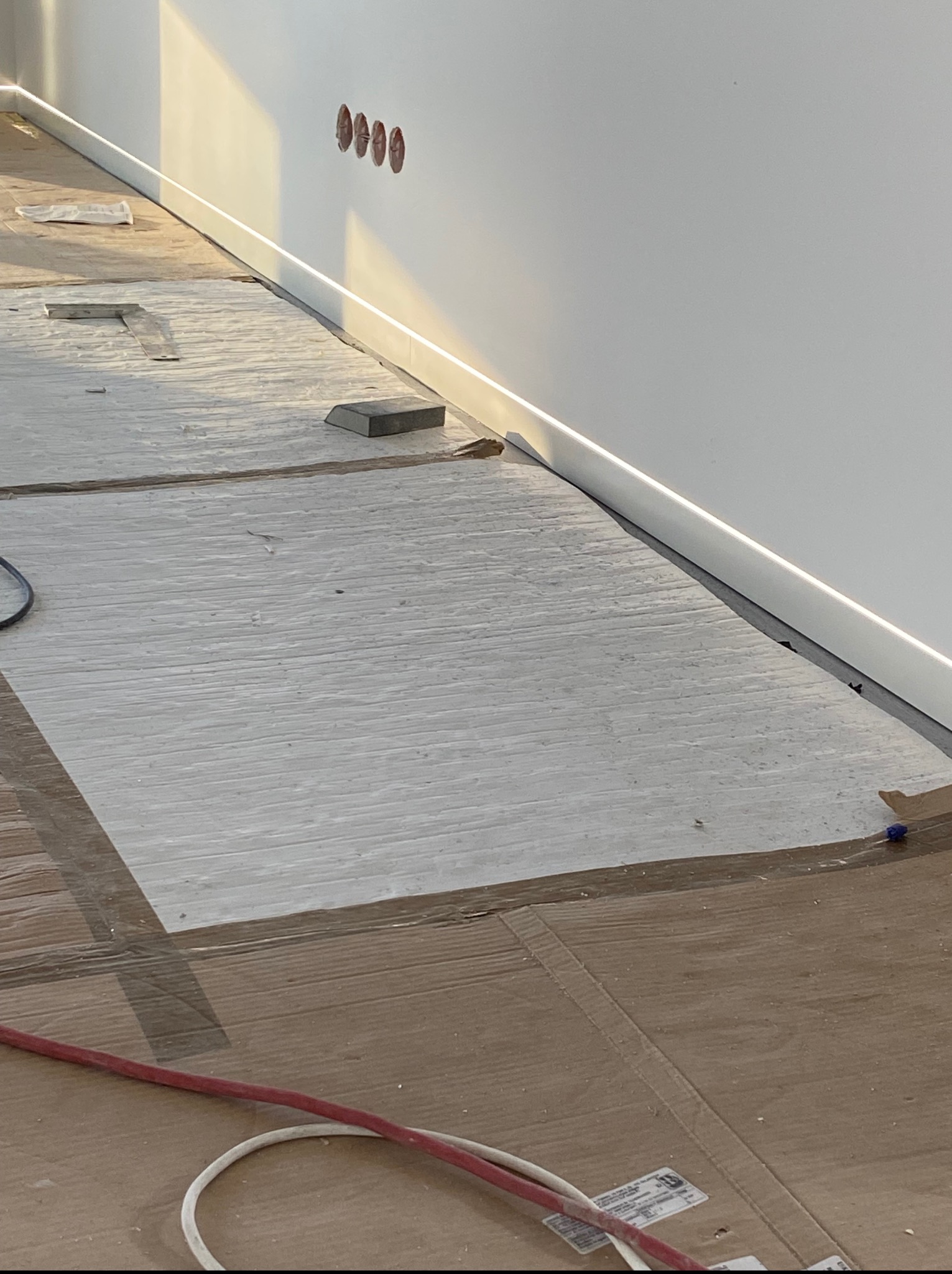 Układanie szarych płytek podłogowych z oświetleniem LED przy ścianie. Widoczne narzędzia i kable. Prace wykończeniowe w trakcie realizacji.