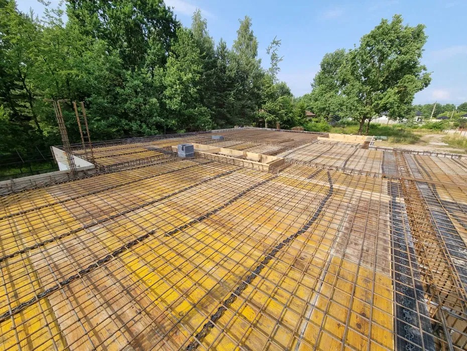 Żółte szalunki stropowe z siatką zbrojeniową na budowie domu, widok z góry na tle zieleni drzew. Zbrojenie stropu przed betonowaniem.