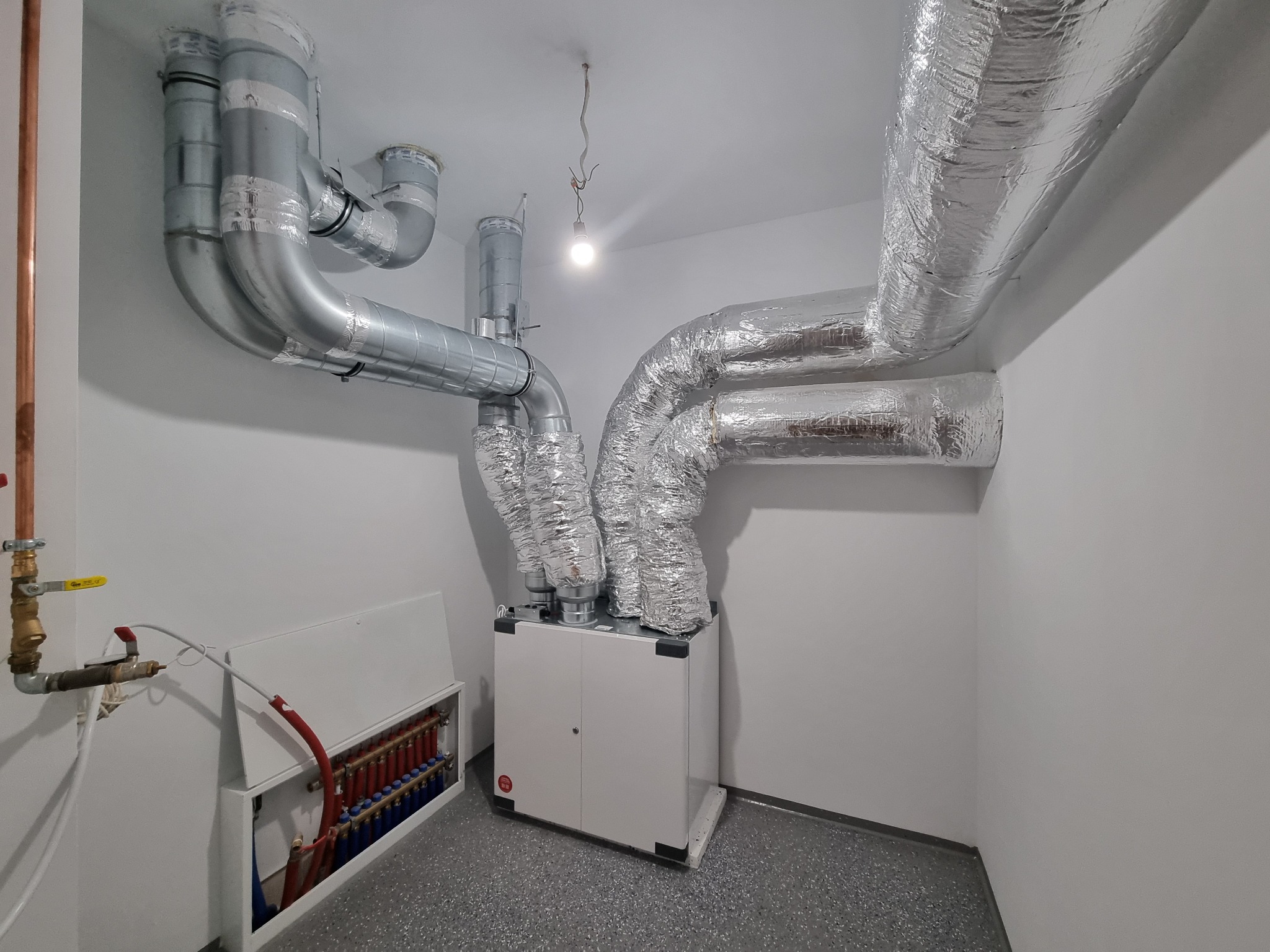 Kompleksowa instalacja rekuperacji z ociepleniem rur i żywicą epoksydową na posadzce. Widoczny rekuperator, rury wentylacyjne i rozdzielacz ogrzewania podłogowego.