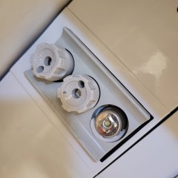 Złota rączka 24h - Białe pokrętła termostatyczne grzejnika, dwa z nich założone, a jeden z metalowym trzpieniem widocznym w gnieździe, na tle białej obudowy grzejnika.