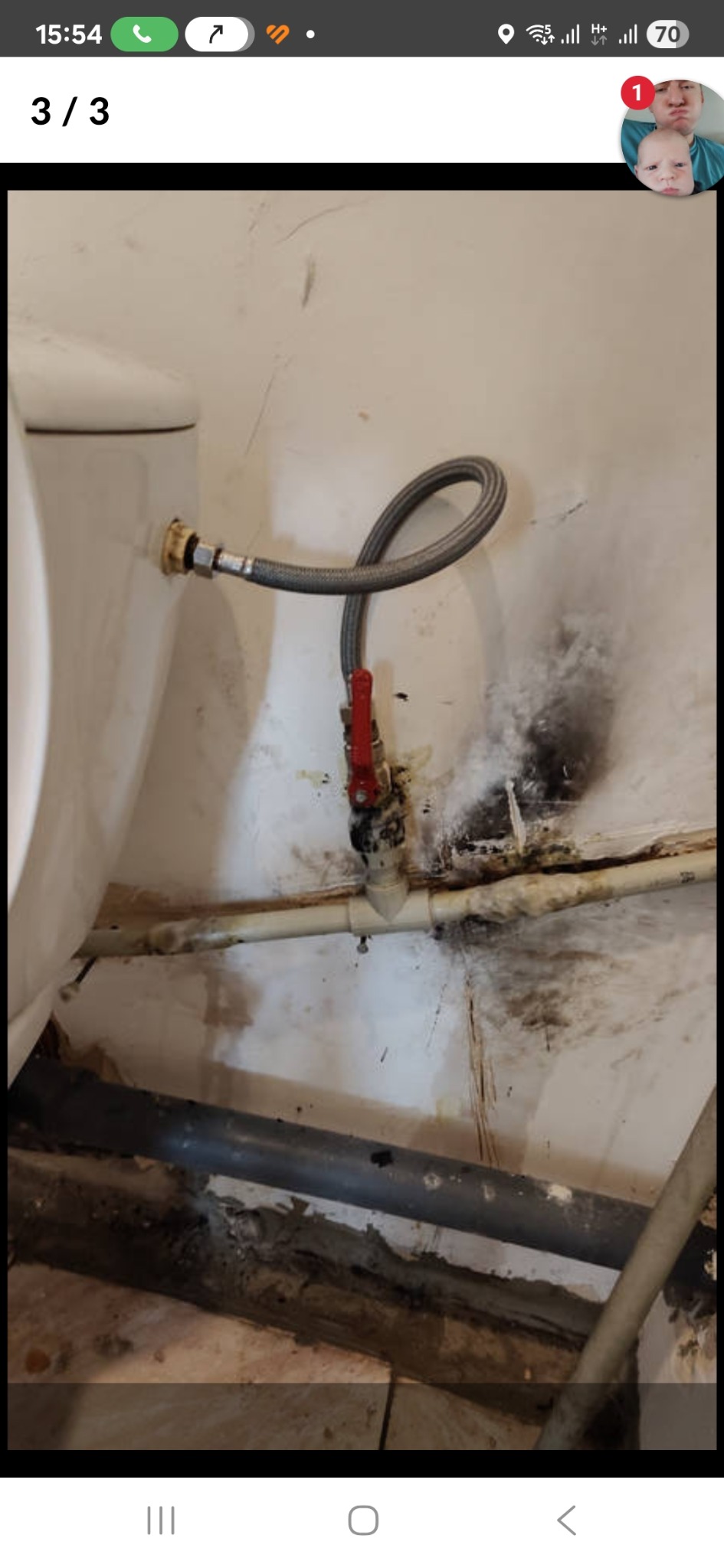 Podłączenie wężyka do toalety z zaworem odcinającym. Widoczne ślady wilgoci i zabrudzeń na ścianie i rurach, co sugeruje potencjalny problem hydrauliczny.