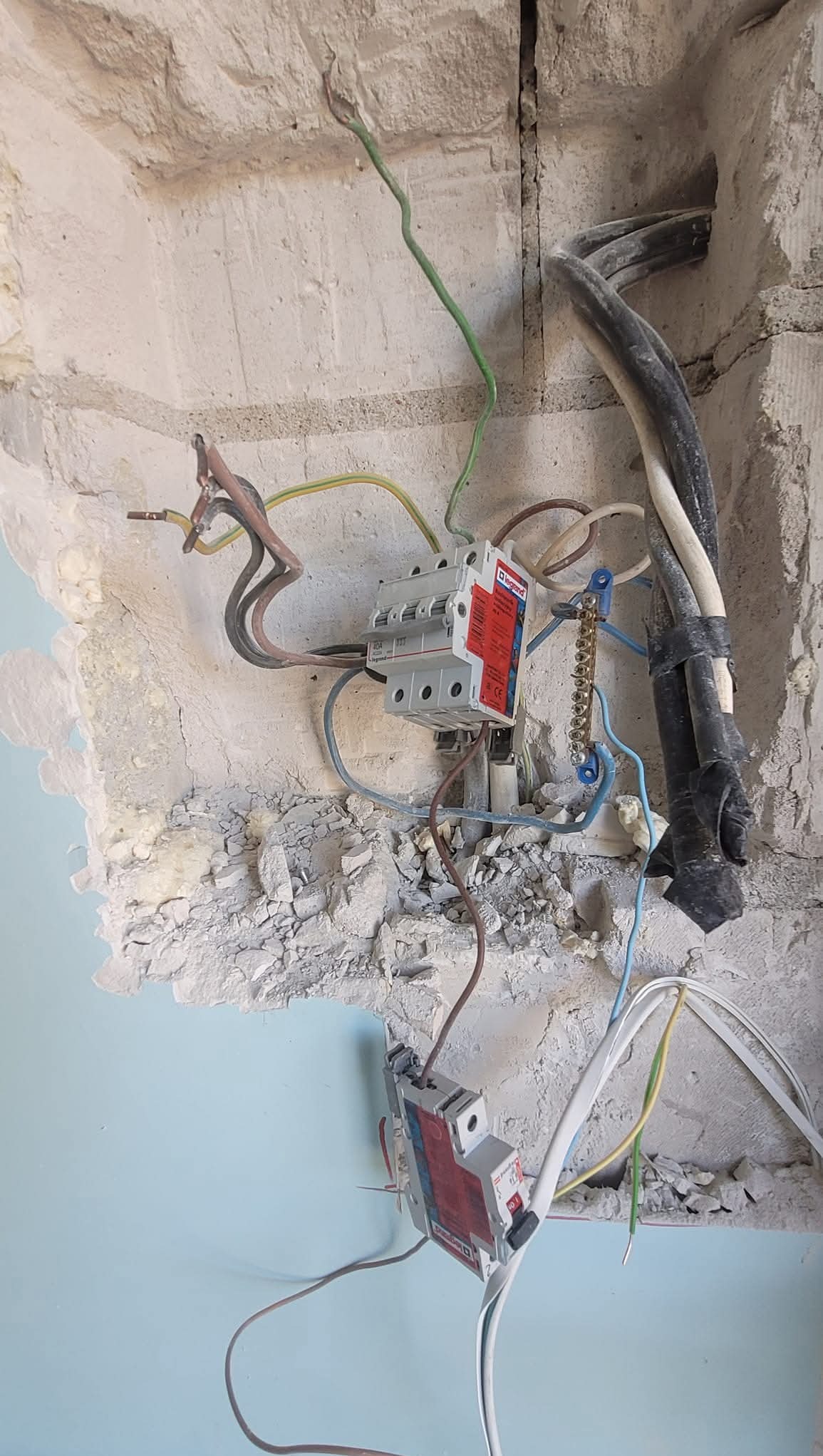 Rozdzielnica elektryczna Legrand z przewodami w surowym otoczeniu ściany. Widoczne kable i elementy instalacji elektrycznej w trakcie montażu w nowym budynku.