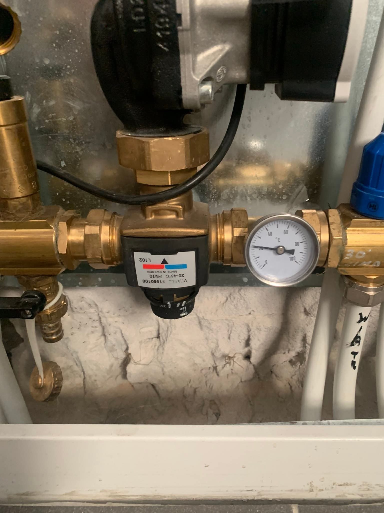 Zamknięty obieg wody z termometrem, zaworem regulacyjnym i pompą obiegową. Widoczne miedziane rury i białe rury z tworzywa sztucznego.