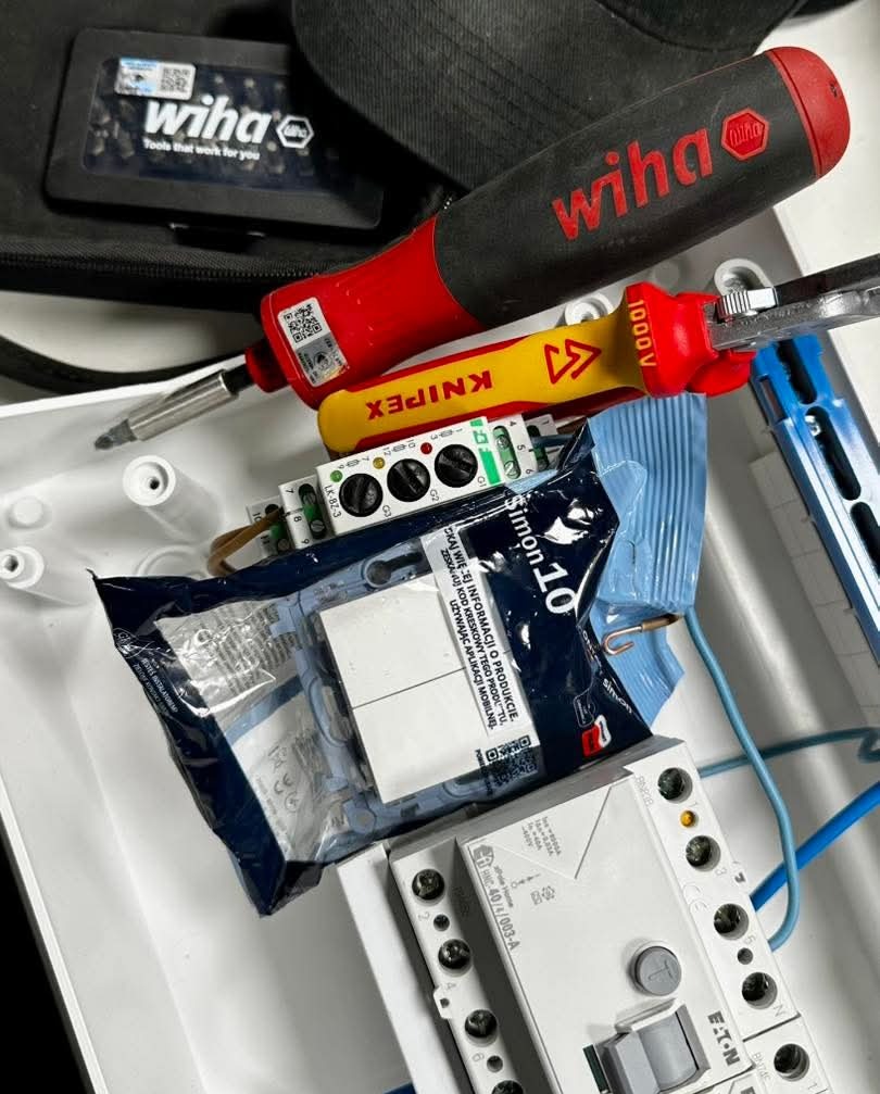 Rozdzielnica elektryczna z narzędziami Wiha i Knipex, widoczne przewody, bezpieczniki Eaton i opakowanie Simon 10, sugerujące prace instalacyjne.