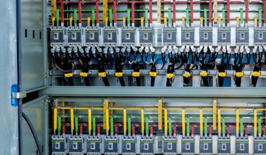 Rozdzielnica elektryczna z bezpiecznikami, okablowaniem w kolorach: żółtym, zielonym i czerwonym. Widoczne czarne przewody z żółtymi oznaczeniami.