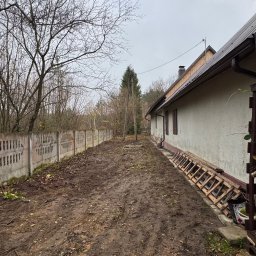 Piotr Babiarz - Przygotowany teren pod zakładanie ogrodu: wyrównana ziemia, widoczny płot betonowy i budynek z drewnianymi elementami. Ślady po wycince drzew.