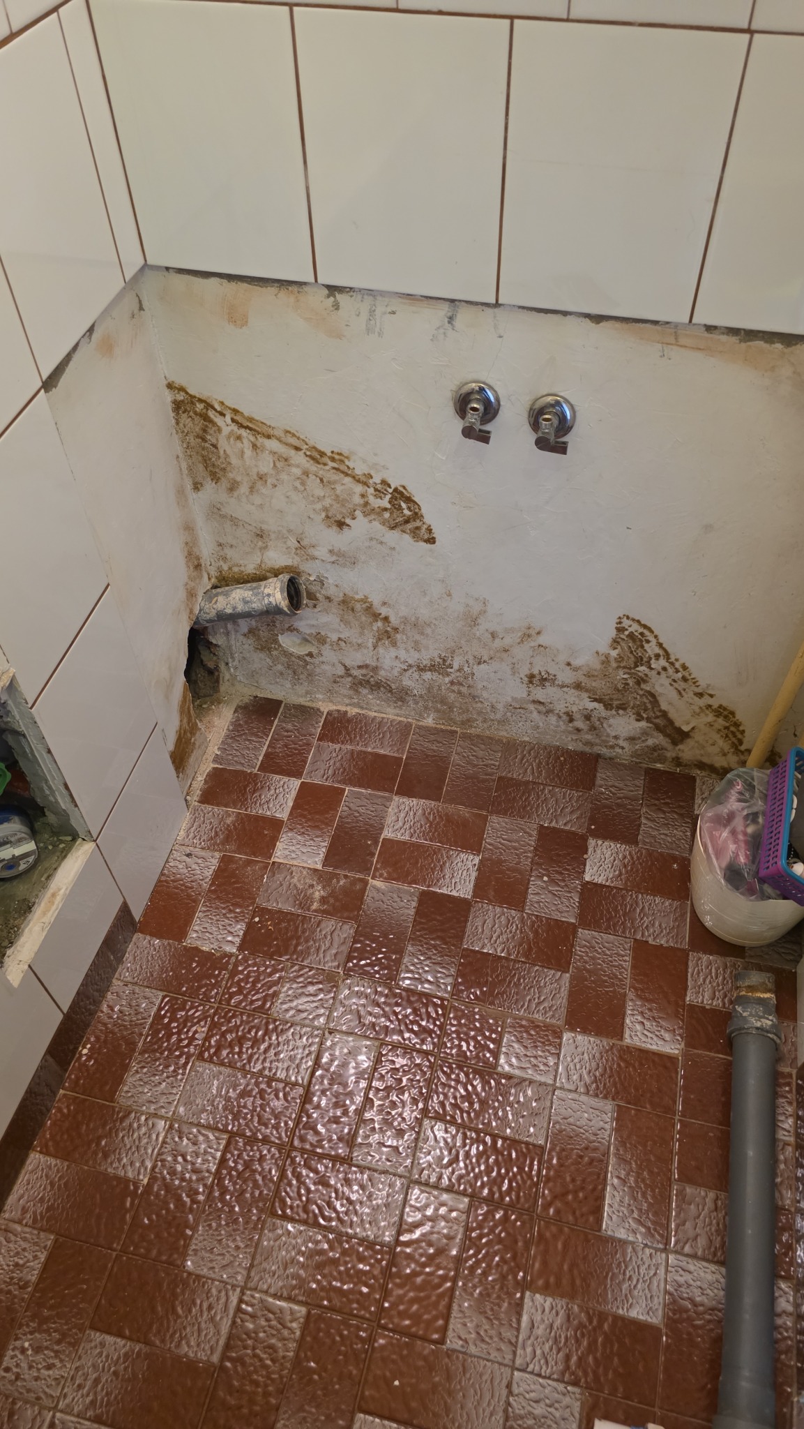 Przygotowanie do montażu armatury w łazience: widoczne rury, płytki i ślady po starej instalacji.  Kątowe ujęcie na remontowaną przestrzeń.