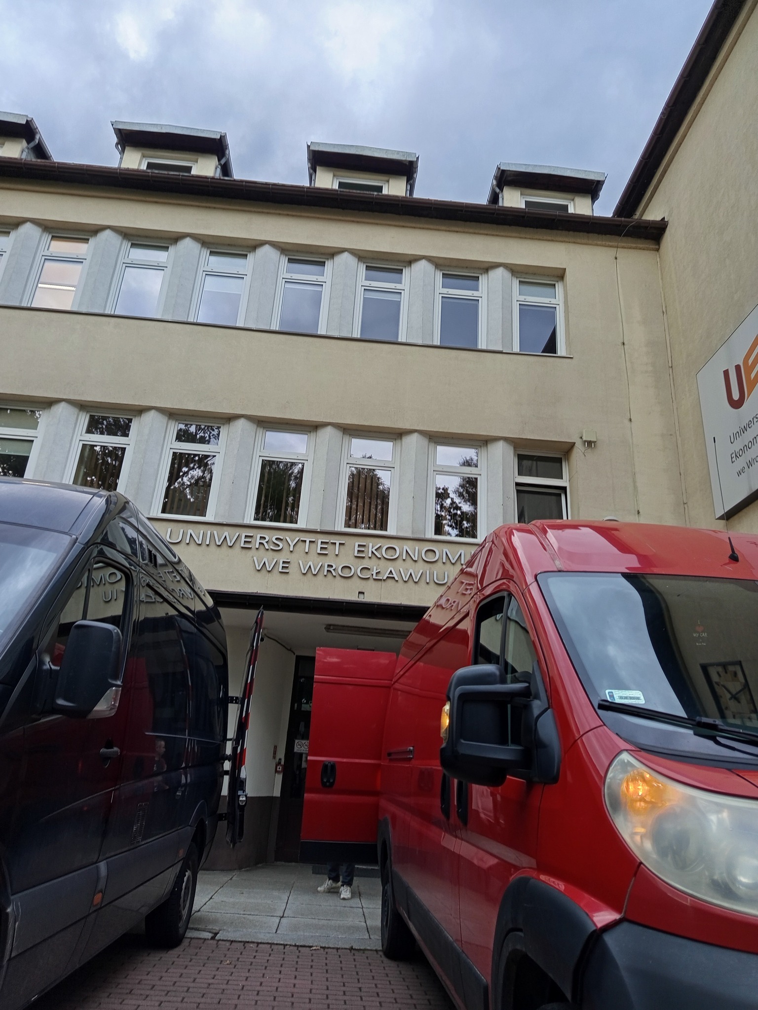 Czerwony i czarny bus przed budynkiem Uniwersytetu Ekonomicznego we Wrocławiu, otwarte drzwi, prawdopodobnie w trakcie przeprowadzki.
